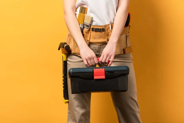Vista cortada de handywoman segurando caixa de ferramentas no fundo amarelo — Fotografia de Stock
