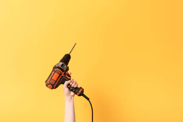 Vista recortada de la mujer sosteniendo taladro sobre fondo amarillo — Stock Photo