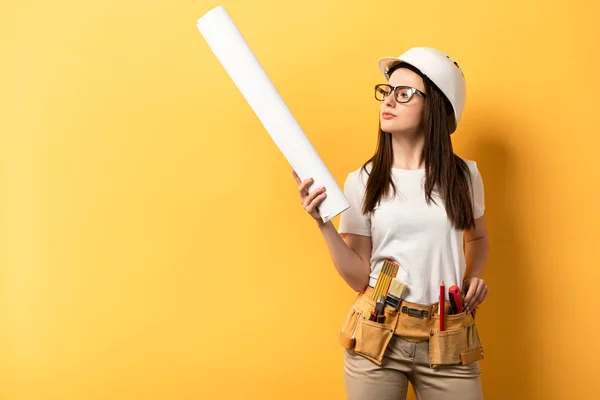 Premuroso tuttofare in possesso e guardando cianografia su sfondo giallo — Foto stock