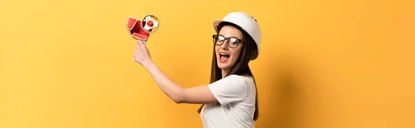 Tiro panorâmico de handywoman chocado segurando dispensador de fita no fundo amarelo — Fotografia de Stock