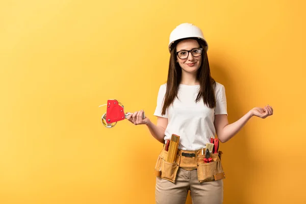 Femme à tout faire souriante avec distributeur de ruban adhésif regardant la caméra sur fond jaune — Photo de stock