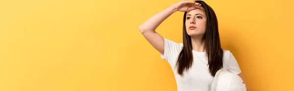 Panoramic shot of serious handywoman holding helmet and looking away on yellow background — Stock Photo