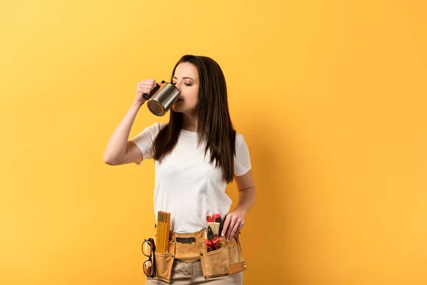 Attractive handywoman drinking tea on yellow background with copy space — Stock Photo