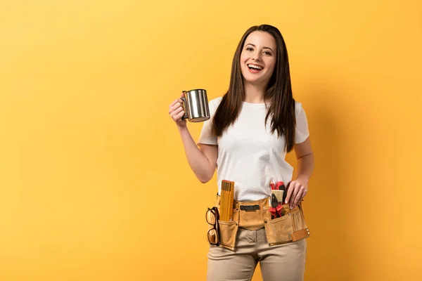 Smiling handywoman holding metal cup on yellow background — Stock Photo