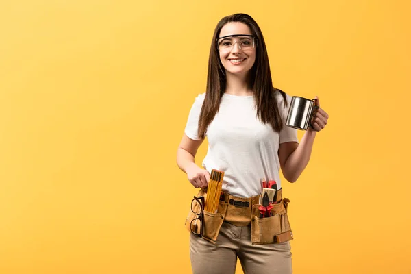 Smiling handywoman holding metal cup and looking at camera isolated on yellow — Stock Photo