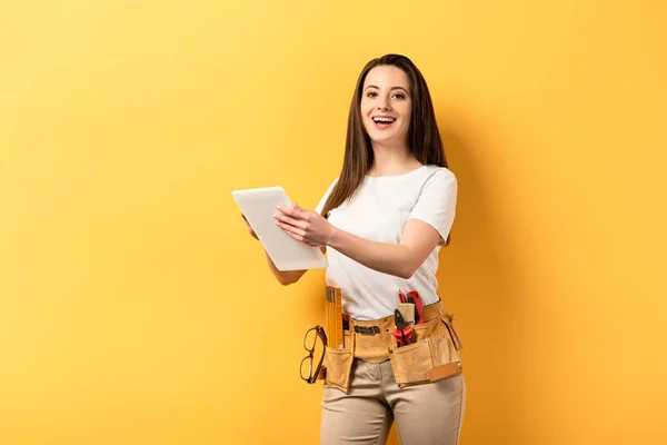 Smiling handywoman holding digital tablet on yellow background with copy space — Stock Photo