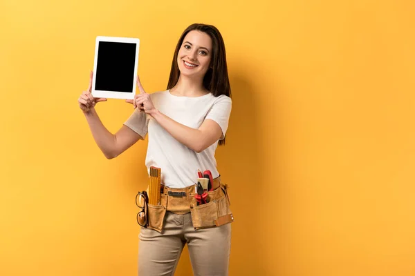 Femme à tout faire souriante tenant tablette numérique avec espace de copie sur fond jaune — Photo de stock