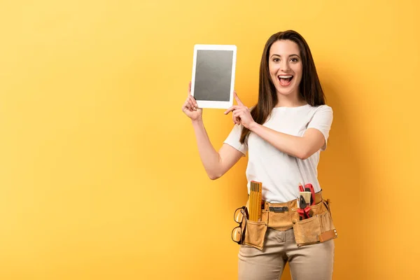 Shocked handywoman holding digital tablet with copy space on yellow background — Stock Photo
