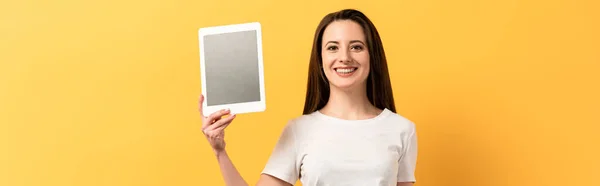 Plano panorámico de mujer sonriente sosteniendo tableta digital sobre fondo amarillo - foto de stock