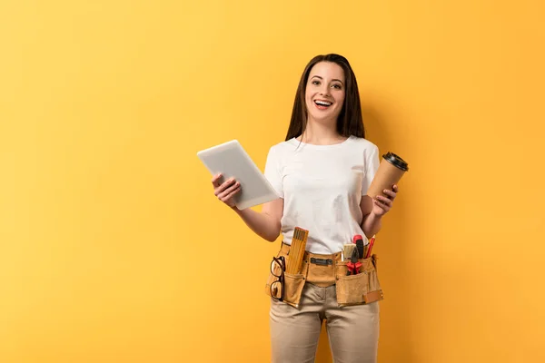 Lächelnde Handarbeiterin mit Pappbecher und digitalem Tablet auf gelbem Hintergrund — Stockfoto
