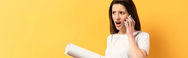 Plano panorámico de la mujer conmocionada hablando en el teléfono inteligente y la celebración de proyecto sobre fondo amarillo - foto de stock