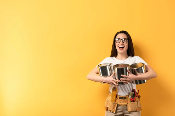 Chocada reparadora segurando latas de tinta e olhando para o fundo amarelo — Fotografia de Stock