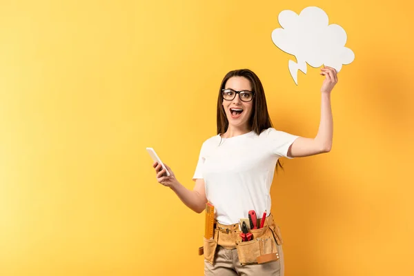 Reparadora impactada sosteniendo teléfono inteligente y burbuja de pensamiento sobre fondo amarillo — Stock Photo