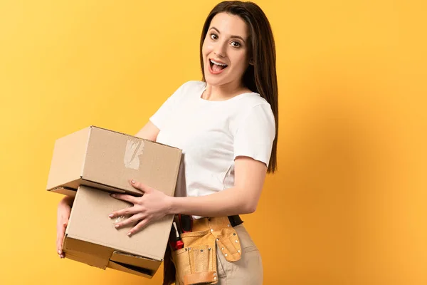 Chocado reparadora segurando caixas de papelão no fundo amarelo — Fotografia de Stock