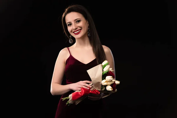 Smiling woman in dress holding bouquet isolated on black — Stock Photo
