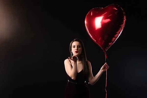 Frau im Kleid mit herzförmigem Luftballon und Luftkuss auf schwarzem Hintergrund — Stockfoto