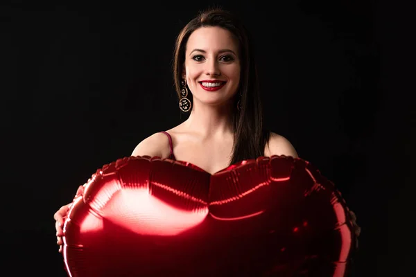 Femme souriante tenant ballon en forme de coeur dans 14 février isolé sur noir — Photo de stock