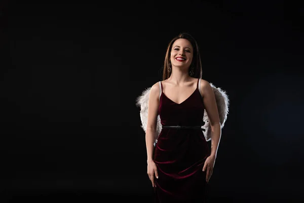 Mujer sonriente en vestido con alas mirando a la cámara aislada en negro - foto de stock