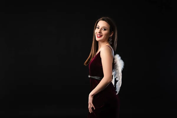 Mujer sonriente en vestido con alas mirando a la cámara aislada en negro - foto de stock