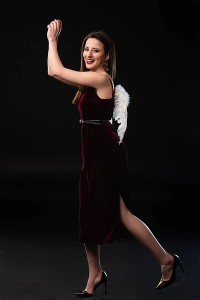 Smiling woman in dress with wings looking at camera and walking on black background — Stock Photo