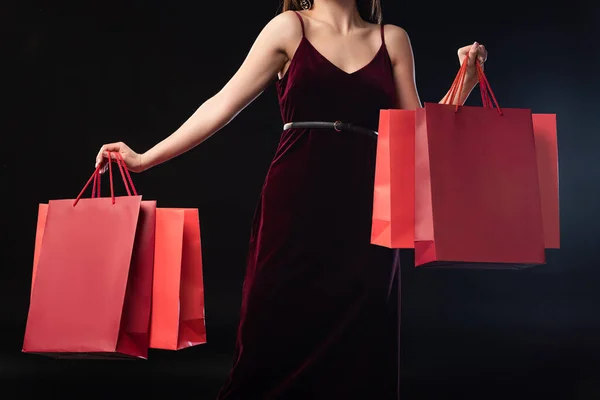 Cropped view of woman in dress holding shopping bags on black background — Stock Photo