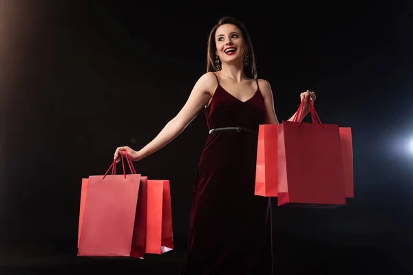 Mulher sorrindo no vestido segurando sacos de compras no fundo preto — Fotografia de Stock
