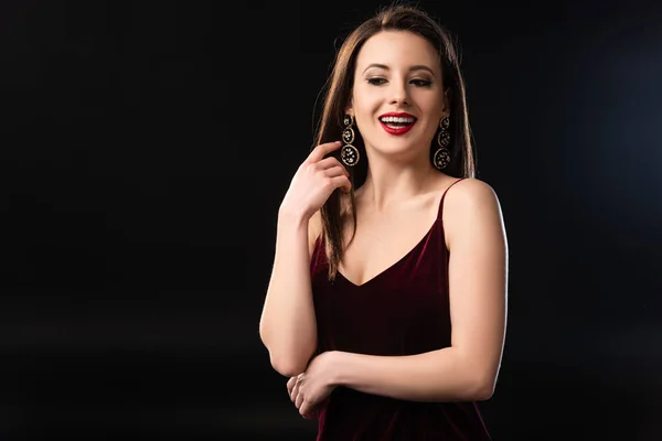 Smiling woman in dress with earrings looking away on black background — Stock Photo