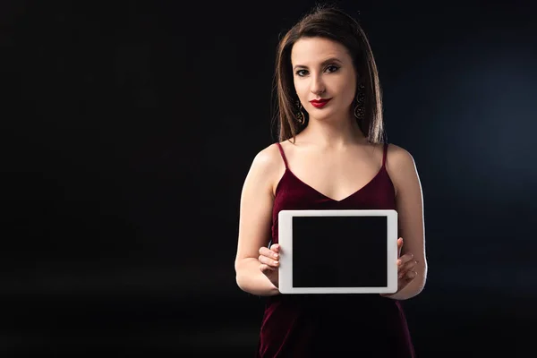 Femme sérieuse en robe tenant tablette numérique sur fond noir — Photo de stock