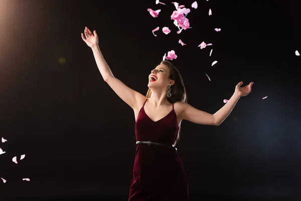 Sorrindo mulher no vestido de pé perto de cair confete no fundo preto — Fotografia de Stock