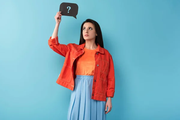 Thoughtful woman holding speech bubble with question sign on blue background — Stock Photo