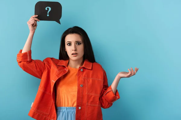 Schockierte Frau hält Sprechblase mit Fragezeichen auf blauem Hintergrund — Stockfoto