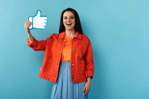 Smiling woman in jacket holding paper like on blue background — Stock Photo