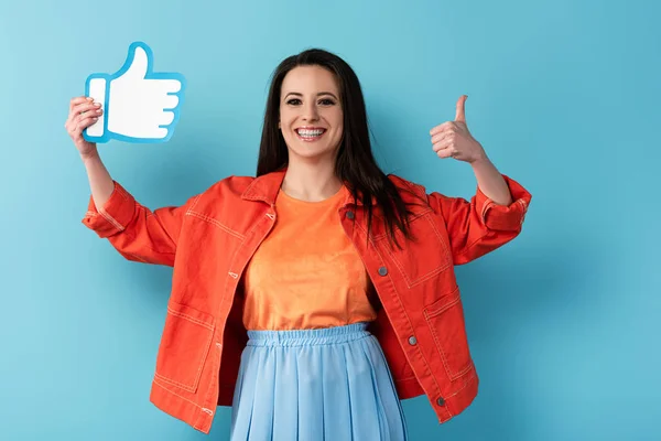 Sorrindo mulher mostrando polegar para cima e segurando papel como no fundo azul — Fotografia de Stock