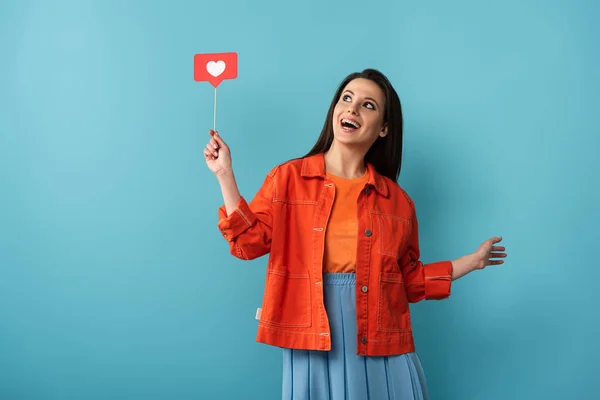 Schockierte Frau hält Stock mit Papier wie auf blauem Hintergrund — Stockfoto