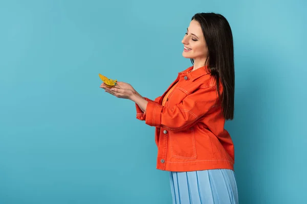 Side view of smiling woman holding paper butterfly on blue background — Stock Photo