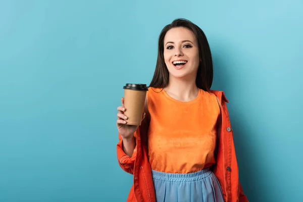 Mulher sorrindo segurando copo de papel com café no fundo azul — Fotografia de Stock