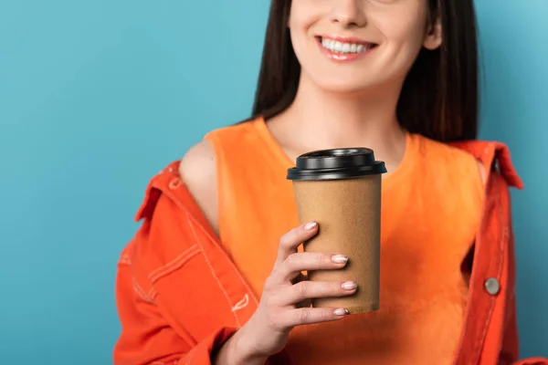 Vista recortada de la mujer sonriente sosteniendo taza de papel con café sobre fondo azul — Stock Photo