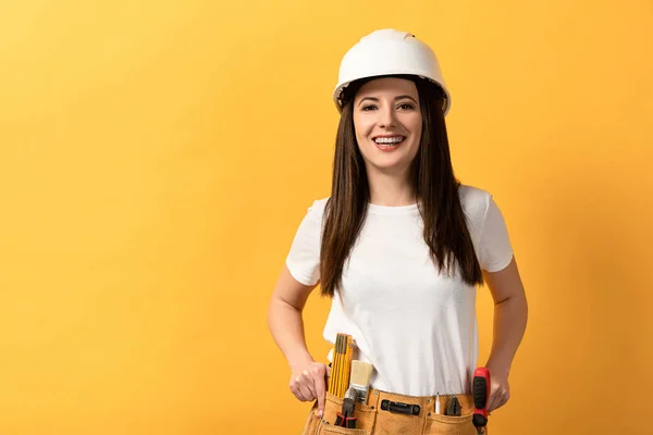 Smiling handywoman in helmet looking at camera on yellow background — Stock Photo