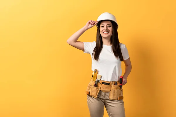 Sorrindo handywoman no capacete olhando para a câmera no fundo amarelo — Fotografia de Stock