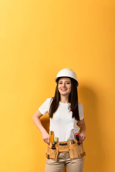 Lächelnde Handarbeiterin mit Helm blickt in die Kamera auf gelbem Hintergrund — Stockfoto