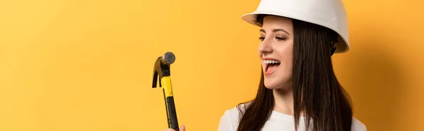 Panoramic shot of smiling handywoman holding hammer on yellow background — Stock Photo