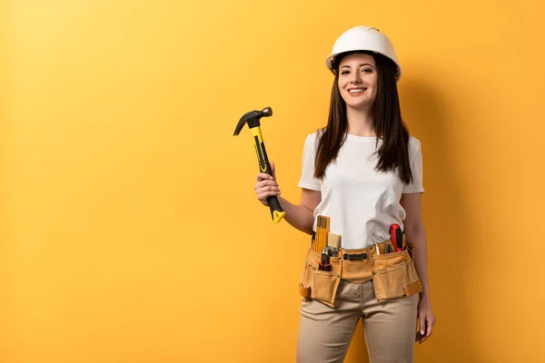 Lächelnde Handarbeiterin im Helm mit Hammer auf gelbem Hintergrund — Stockfoto