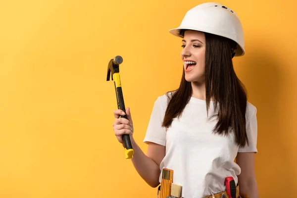 Smiling handywoman in helmet holding hammer on yellow background — Stock Photo