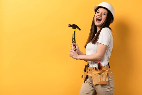 Sorridente tuttofare in casco tenendo martello su sfondo giallo — Foto stock