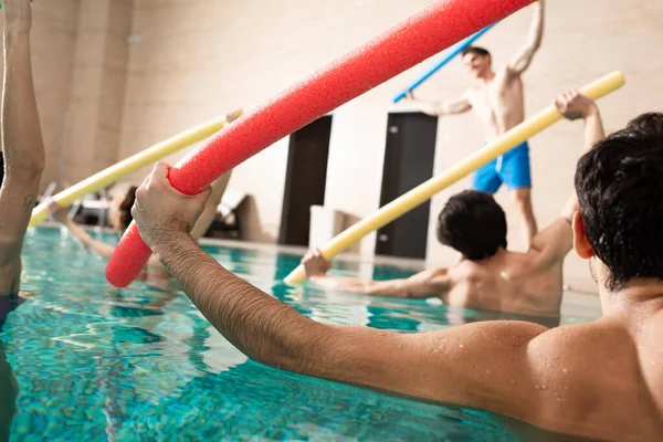 Enfoque selectivo de personas entrenando con fideos de piscina durante aeróbicos acuáticos en piscina - foto de stock