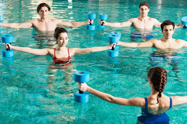 Trainer holding barbells while exercising with group of young people in swimming pool — Stock Photo