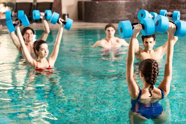 Selective focus of trainer holding barbells while exercising water aerobics with people in swimming pool — Stock Photo