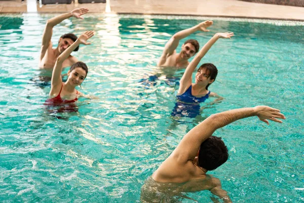 Entrenador haciendo ejercicio con gente sonriente durante aeróbic acuático en la piscina - foto de stock