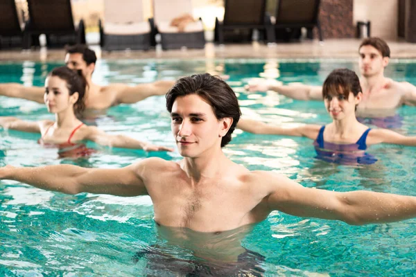 Selective focus of handsome trainer exercising with group of people in swimming pool — Stock Photo