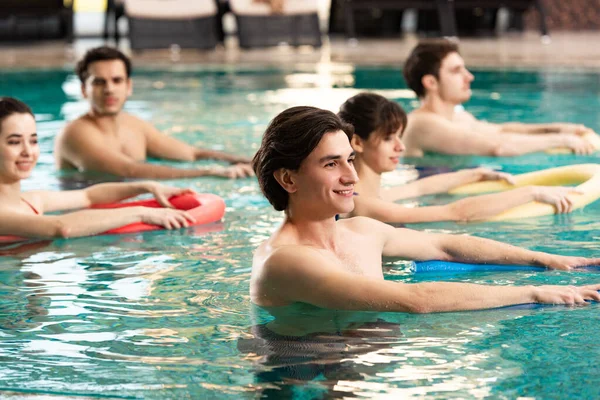 Vista lateral de personas sonrientes con entrenamiento de fideos en la piscina - foto de stock